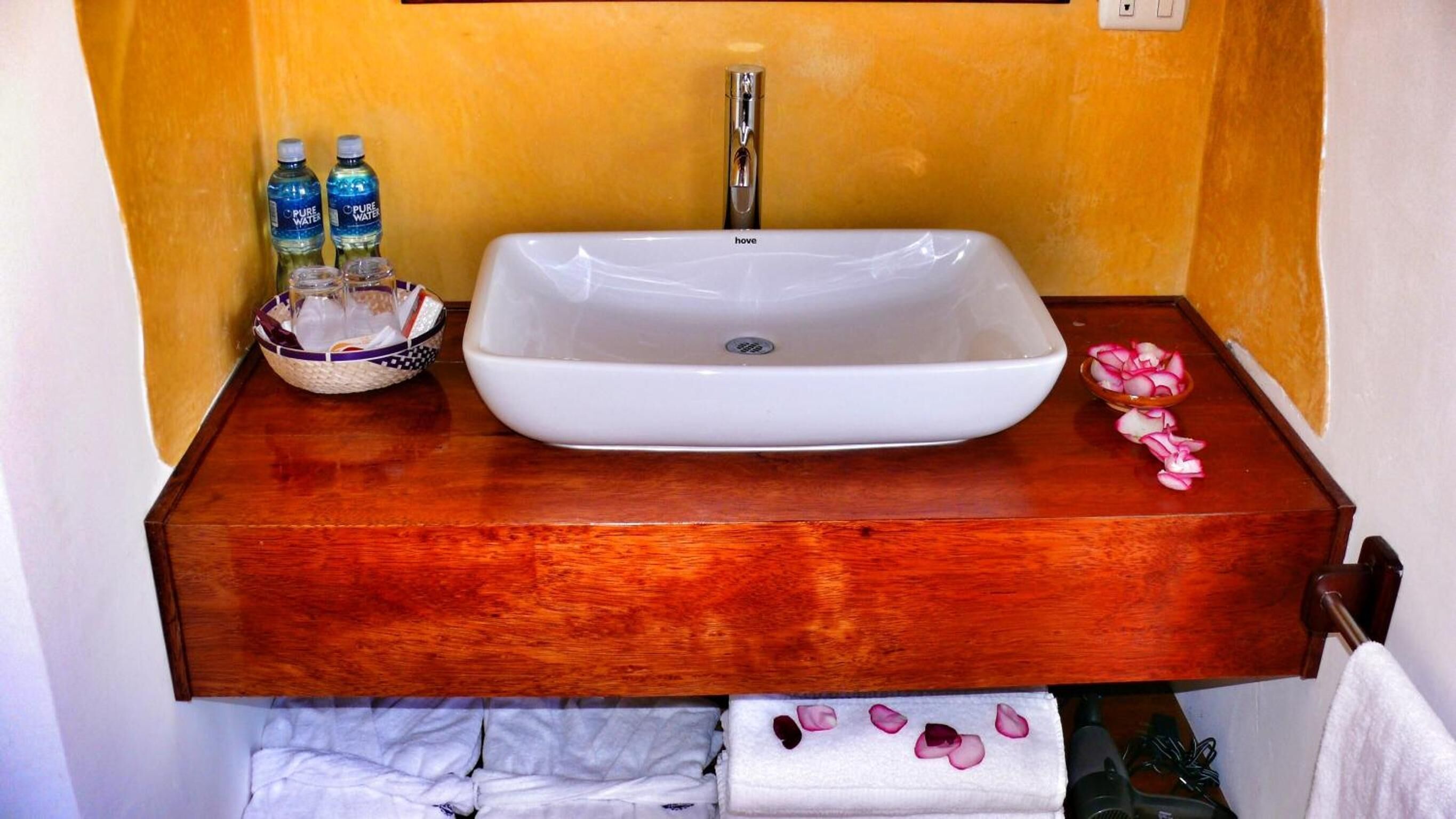 A bathroom with a white sink, two bottles of water, a bowl with a straw, and a towel rack with a towel.