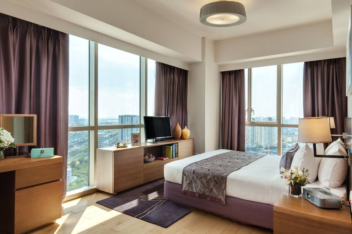 Et moderne hotelværelse med en stor seng, et skrivebord med en computer, et fjernsyn og udsigt til byen gennem store vinduer.