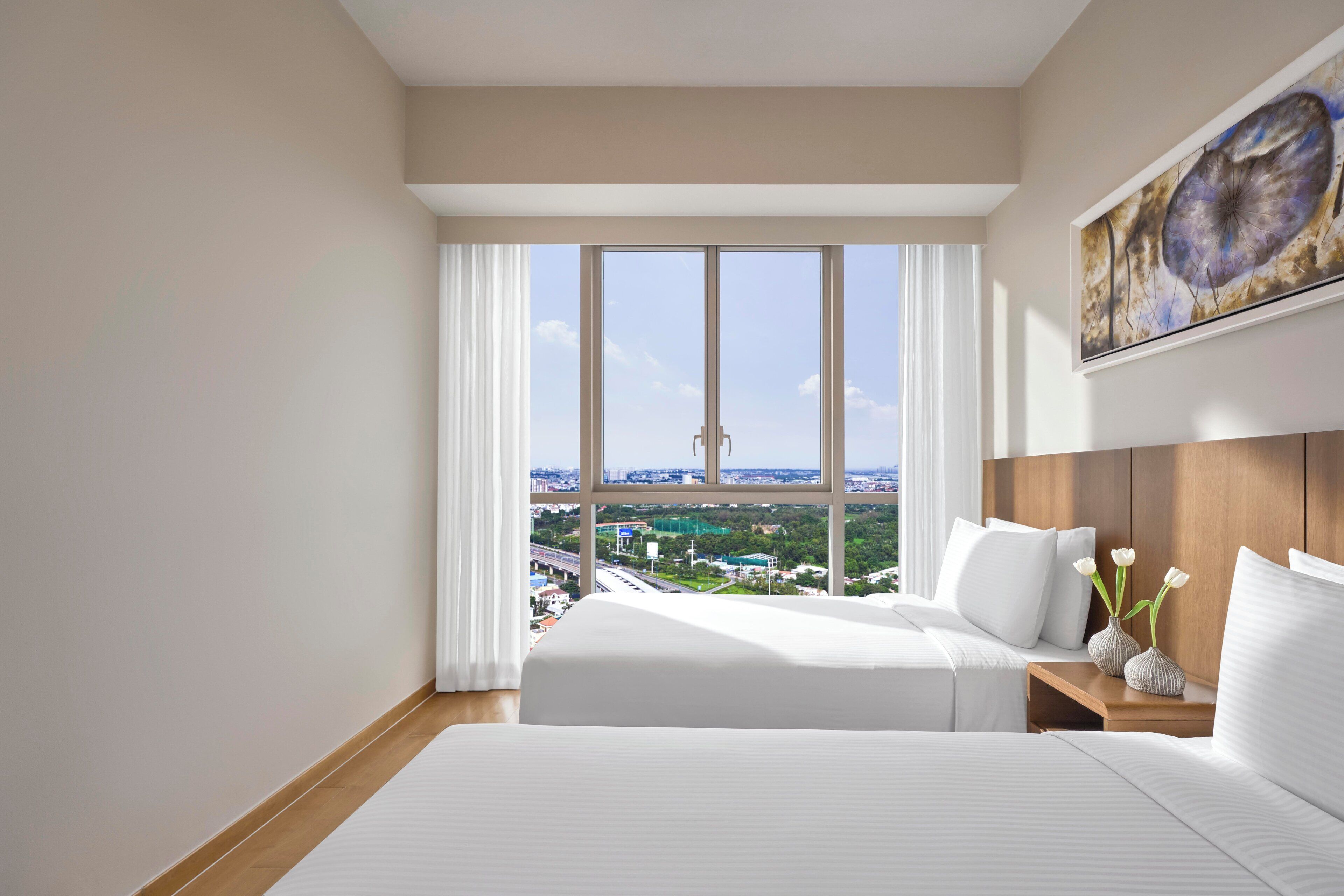 Una habitación de hotel con dos camas, un ventanal con vista a la ciudad y un cuadro en la pared.