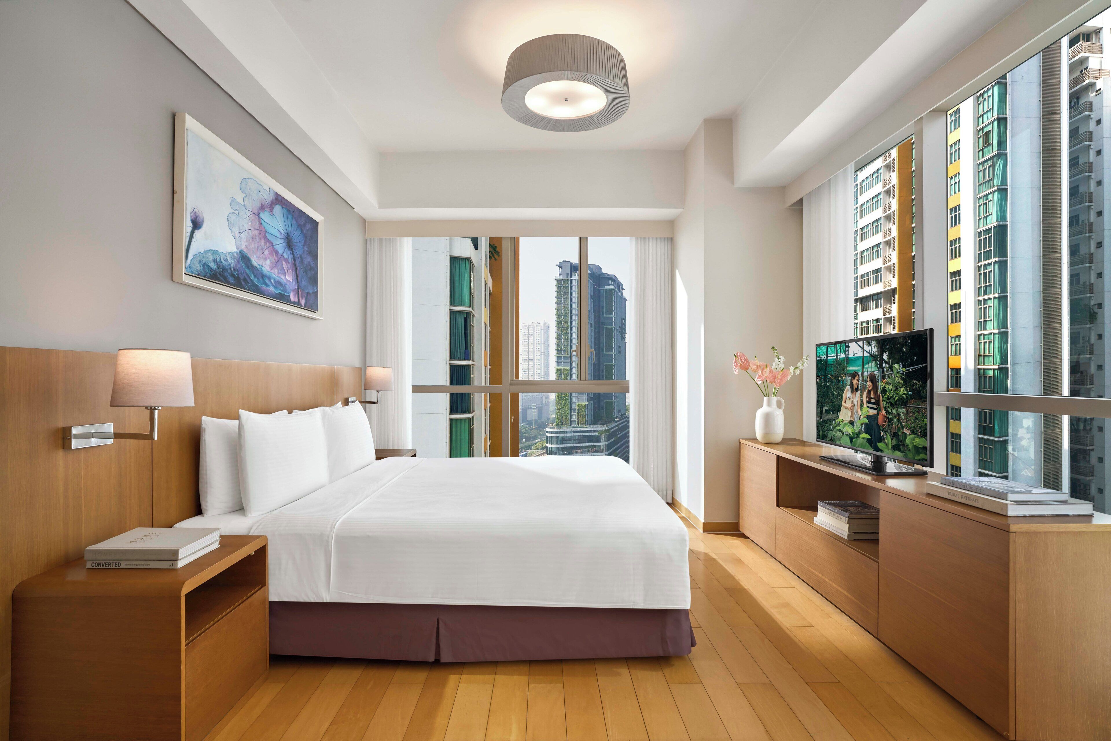 A modern hotel room with a large bed, a TV, and a view of tall buildings.