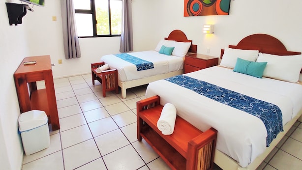 A hotel room with two beds, a TV, a painting, and a window with curtains. - Fragata Departamentos (Puerto Morelos)
