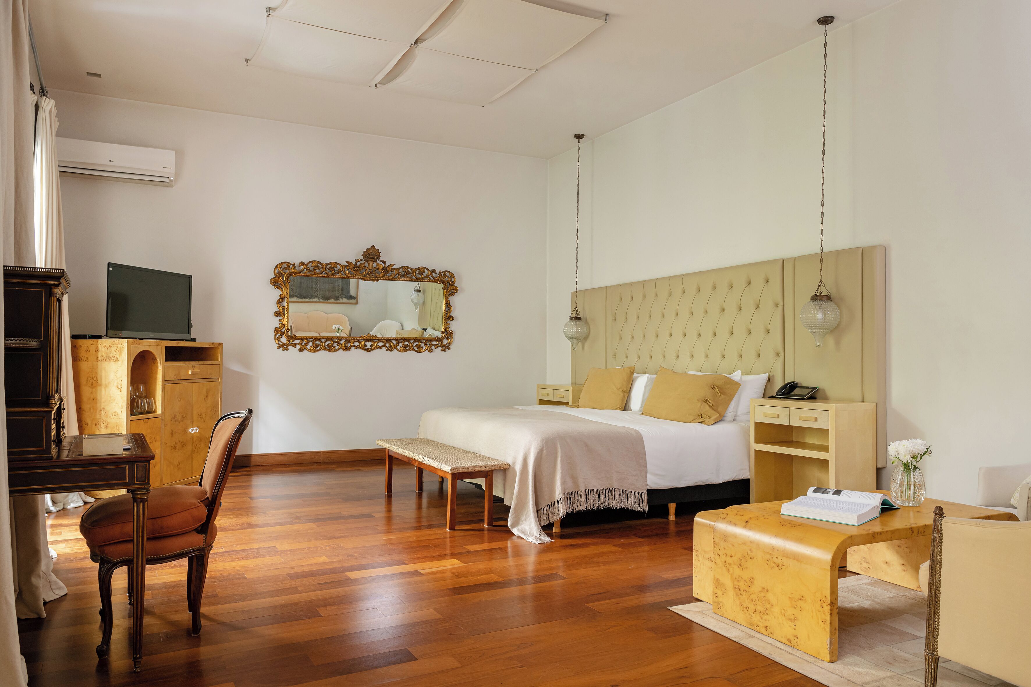 Habitación de hotel con cama, mesita de noche, silla, escritorio y un espejo grande en la pared.