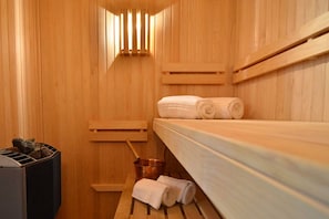 A wooden sauna room with benches, a bench with a bucket, and towels on a bench. - Hub Porteño (Buenos Aires)