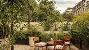 Eine Terrasse mit Tisch und Stühlen, umgeben von Topfpflanzen und einem Backsteinboden.