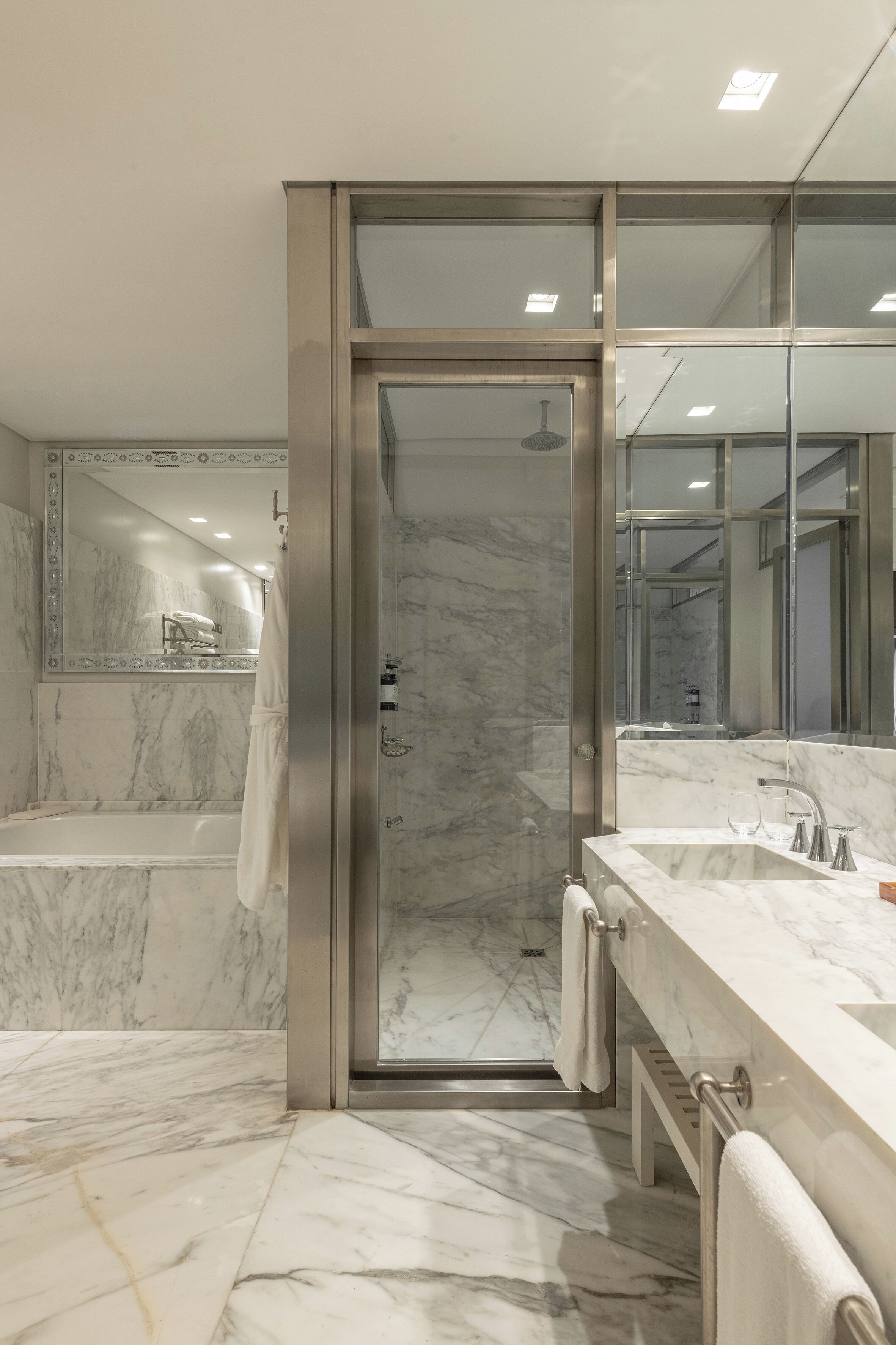 A modern bathroom with a glass-enclosed shower, a marble-tiled floor, and a large mirror above the sink.