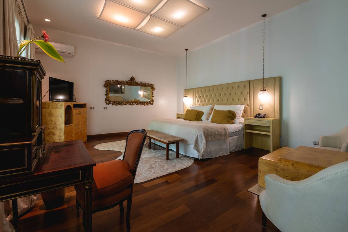 A hotel room with a bed, a desk, a chair, a television, a mirror, and a window.