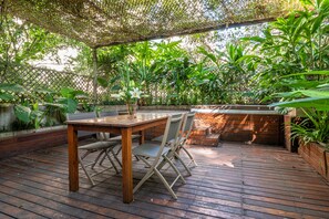 An outdoor patio with a wooden table and chairs, surrounded by lush greenery and a wooden deck. - Hub Porteño (Buenos Aires)