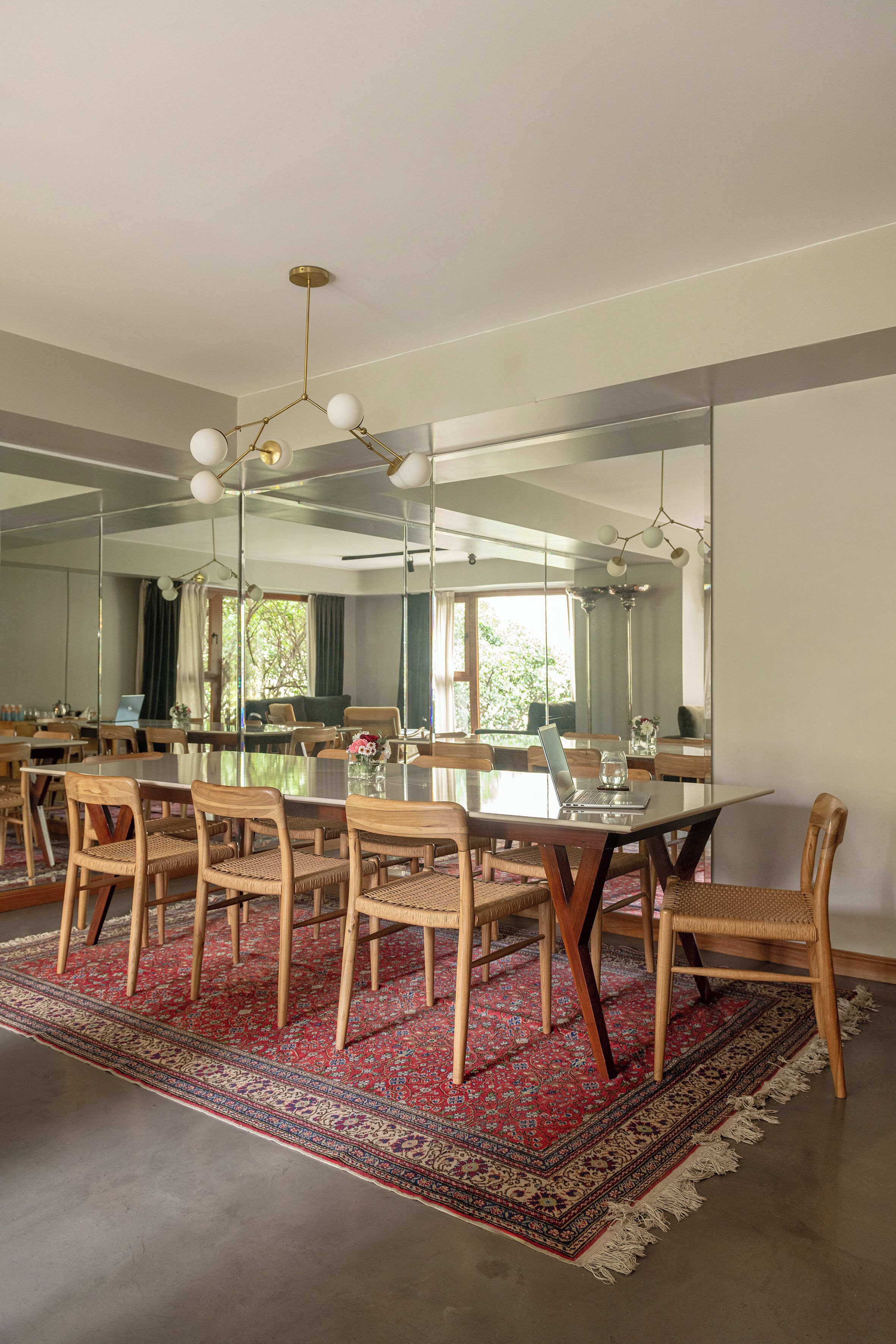 A dining area with a glass table, wooden chairs, a red patterned rug, and a large mirror on the wall.