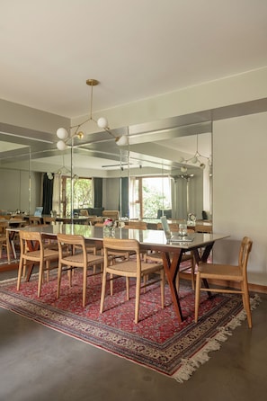 Un coin repas avec une table en verre, des chaises en bois, un tapis rouge à motifs et un grand miroir au mur.