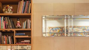 Una sala de estar acogedora con un sofá color beige, un pequeño otoman, una mesa de centro de madera y una estantería llena de libros.