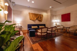 A room with a blue sofa, wooden chairs, a patterned rug, and a large plant. - Hub Porteño (Buenos Aires)