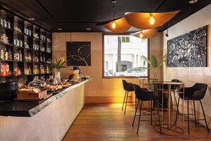 A bar area with a counter displaying food and drinks, a seating area with chairs, and a large window with a view of the street. - Hub Porteño (Buenos Aires)