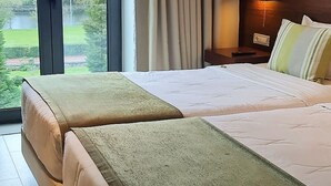 A hotel room with two beds, a large window with curtains, a bedside table with a lamp, and a view of greenery outside. - INATEL Cerveira Hotel (Vila Nova de Cerveira)