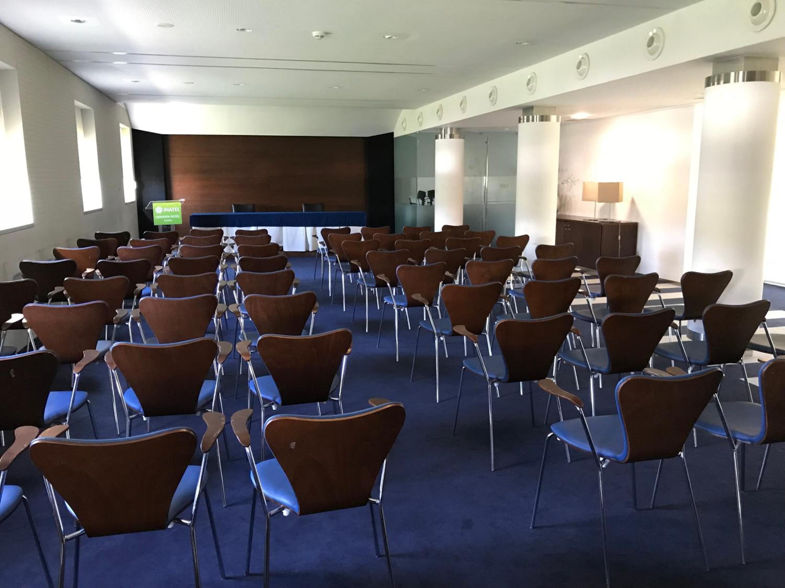 Un salón de conferencias con filas de sillas, un atril y una pantalla de televisión.