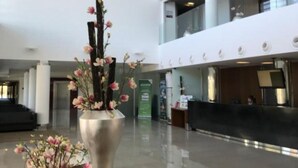 A spacious lobby with a reception desk, a large vase with flowers, and a modern architectural design with glass railings and white pillars. - INATEL Cerveira Hotel (Vila Nova de Cerveira)