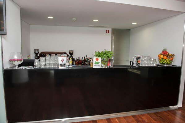 A bar area with a black countertop, glasses, bottles, and a fruit bowl.