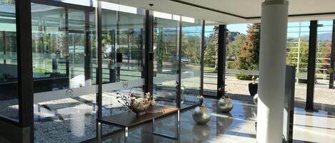 Un interior moderno con grandes ventanales de vidrio, una mesa de madera central con elementos decorativos y un elegante pilar blanco.