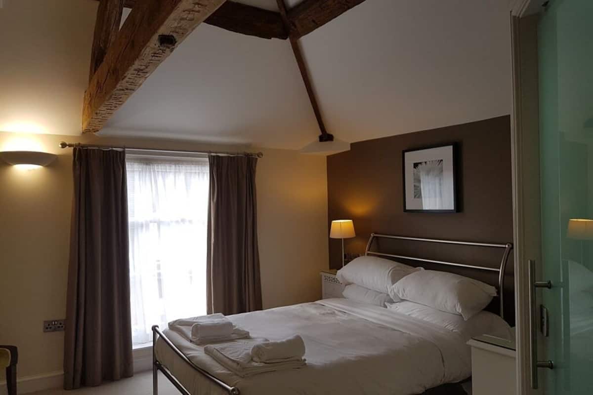 Una camera d'albergo con un letto, un comodino, una lampada, una finestra con tende e un quadro appeso al muro.