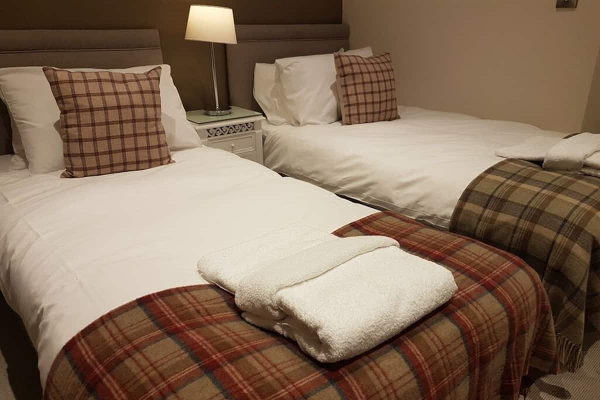 Una camera d'albergo con due letti, ognuno con lenzuola bianche e coperte a quadri. Tra i letti, un comodino con una lampada.