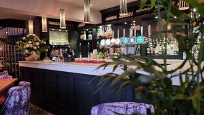 Una zona de bar con mostrador, taburetes, luces colgantes y una estantería para vinos al fondo.