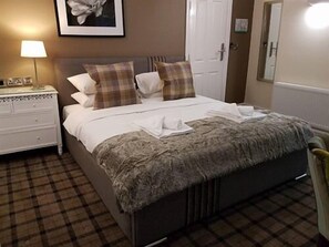 A neatly made bed with a fluffy blanket, a bedside table with a lamp, and a checkered floor. - The Lion Hotel (Stafford)