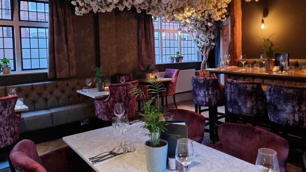 Un restaurante con mesas de mármol, cómodas sillas rojas y un techo decorado con flores blancas.