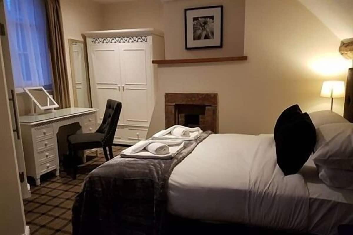 Una camera d'albergo con un letto, una scrivania con una sedia, un armadio, un quadro incorniciato al muro e un caminetto.