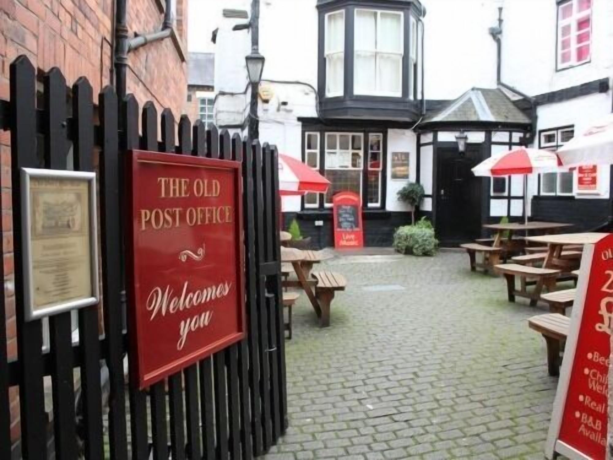 A red sign on a black fence that reads "The Old Post Office" with "Welcome you" below it.
