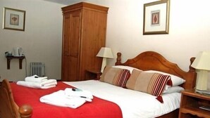 A neatly made bed with a red bedspread, wooden headboard, and striped pillows. There are two bedside tables with lamps, a wooden wardrobe, and framed pictures on the walls. - The Old Post Office (Shrewsbury)