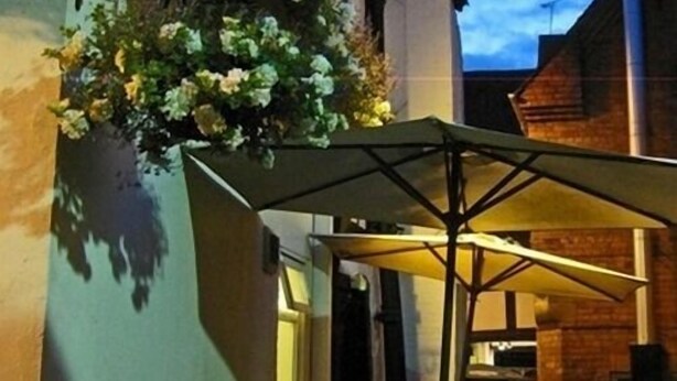 A covered outdoor seating area with a table and chairs, a hanging flower basket, and a brick building in the background. - The Old Post Office (Shrewsbury)