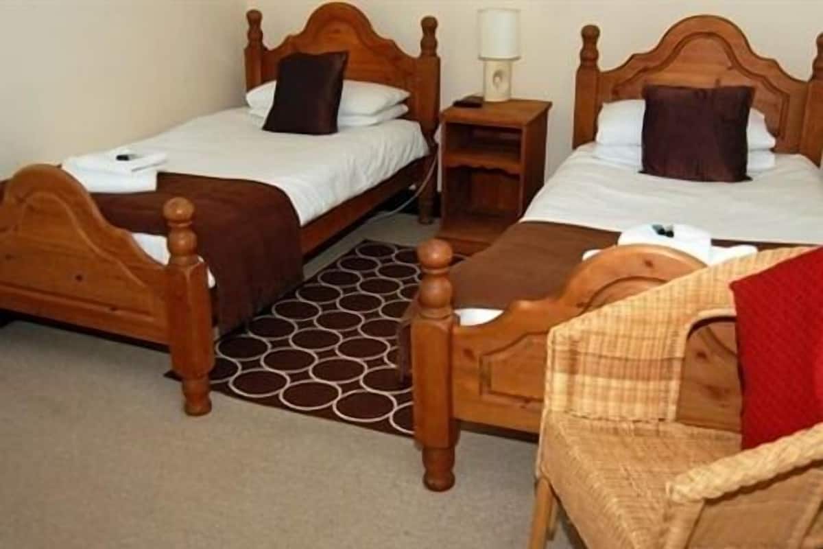 A room with two wooden beds, a small table, and a wicker chair.