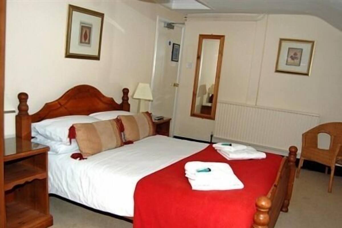 A neatly made bed with a red bedspread, a wooden headboard, and a nightstand with a lamp.