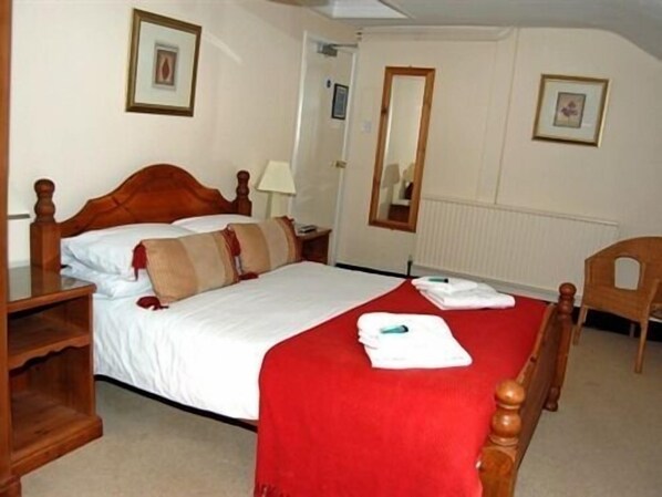 A neatly made bed with a red bedspread, a wooden headboard, and a nightstand with a lamp.