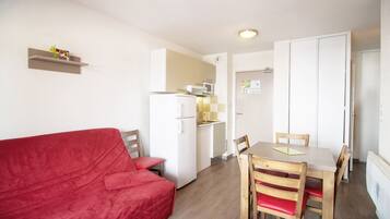 A compact living space with a red sofa, a dining table with chairs, a kitchenette, and a white wardrobe.