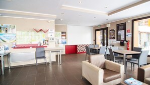 A hotel lobby with a reception desk, seating area, and informational posters on the walls.
