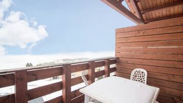 Une terrasse en bois avec une table et des chaises, d’où l’on peut admirer un paysage enneigé et des bâtiments.