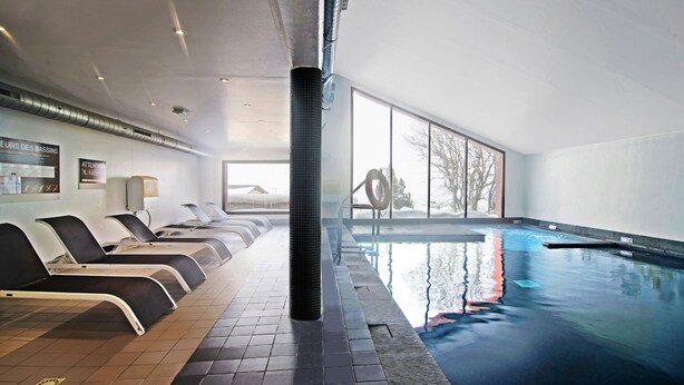 An indoor swimming pool with lounge chairs and a view of trees outside.