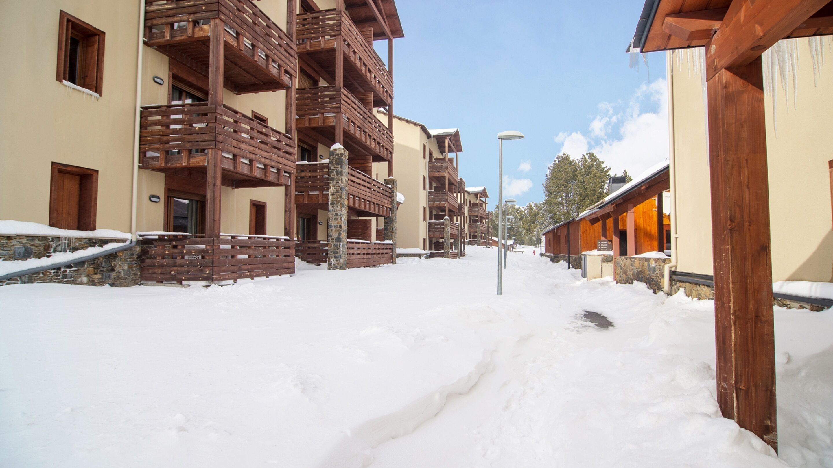 A snow-covered street with wooden buildings, including balconies and a stone wall.