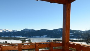 A wooden balcony with a view of snow-covered mountains and a river.