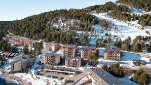 A ski resort with multiple buildings, a parking area, and a snow-covered mountain in the background.