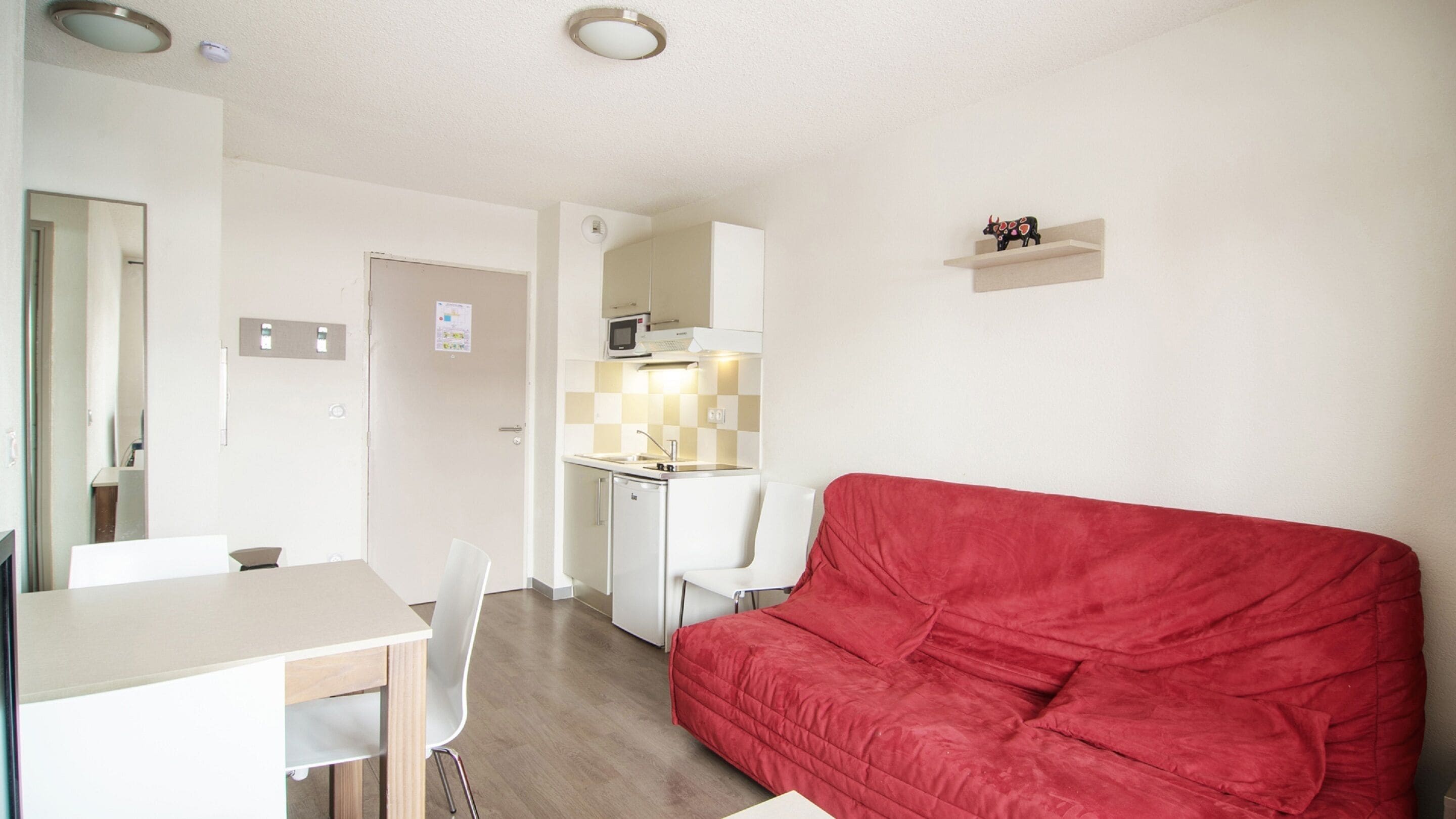 Een ruimtelijk ingerichte leefruimte met een kitchenette, een eethoek en een rode bank.