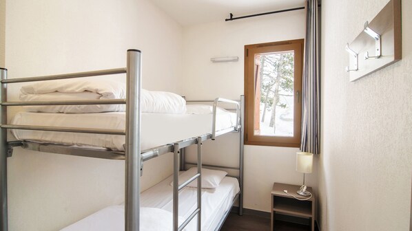 Habitación con literas, una mesita de noche con lámpara y un estante en la pared.