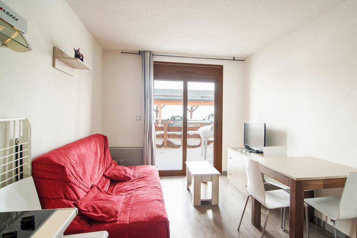 Une pièce de taille modeste, avec un canapé rouge, une petite table sur laquelle se trouve un téléviseur, et une vue sur un espace extérieur enneigé, visible à travers une porte coulissante.