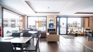 A modern indoor seating area with tables and chairs, large windows, and a view of the outside.