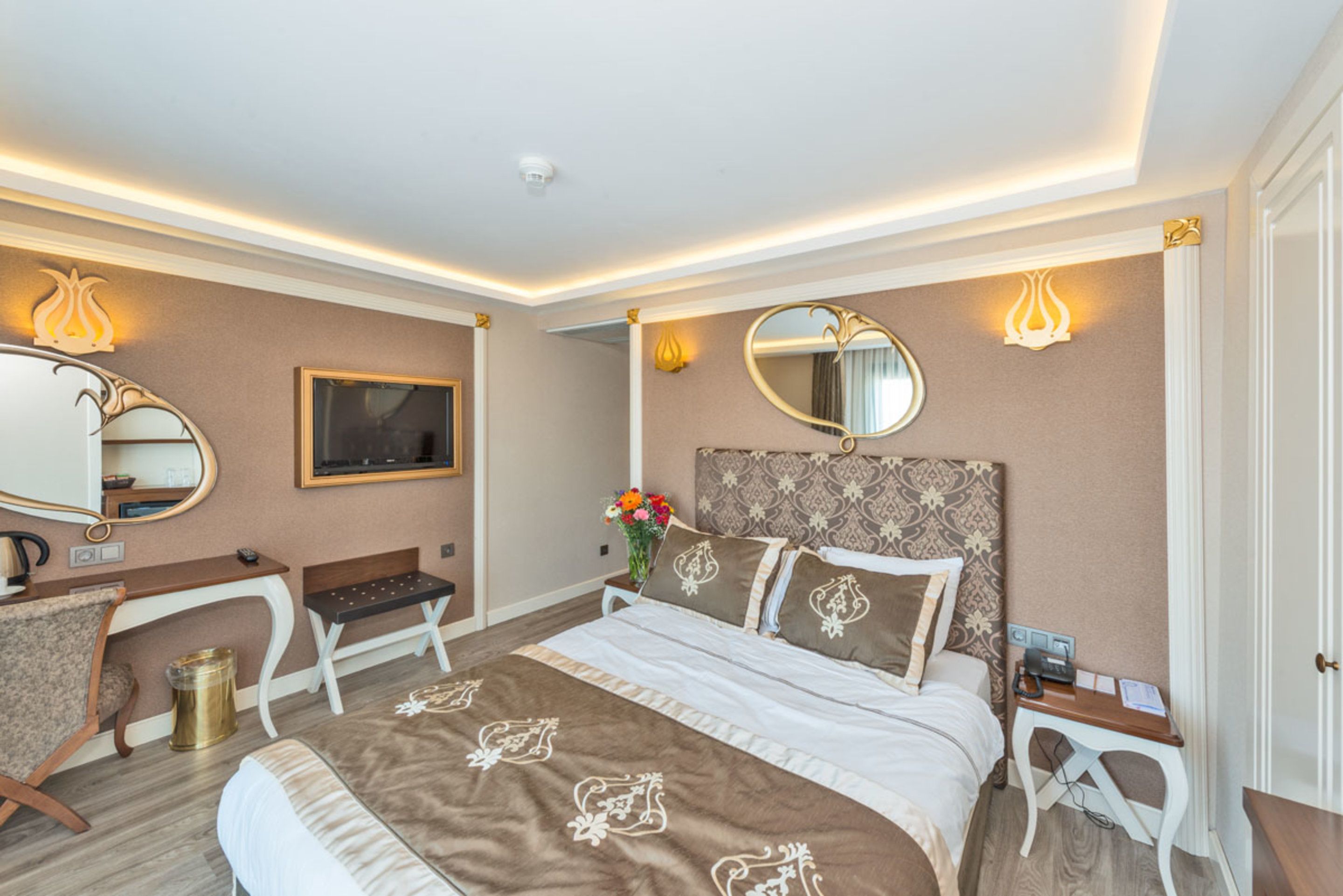 A hotel room with a bed, a desk, a chair, a mirror, and a wall-mounted TV.