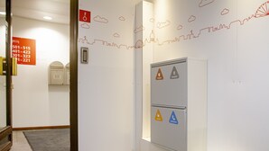 A hallway with a cityscape wall art, a fire alarm, and a trash bin. - Omena Hotel Helsinki City Center (Helsinki)
