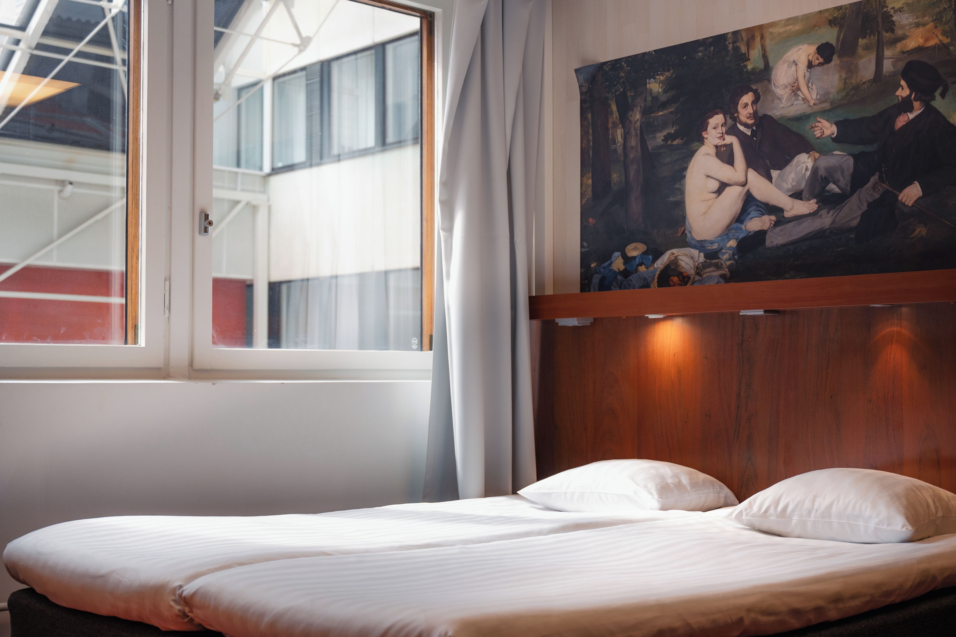 Una habitación de hotel con una cama, un cuadro en la pared y un ventanal con cortinas.