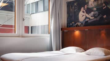 Una habitación de hotel con una cama, un cuadro en la pared y un ventanal con cortinas.