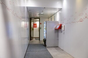A hallway with a glass wall, a red phone station, and a sign with contact numbers.