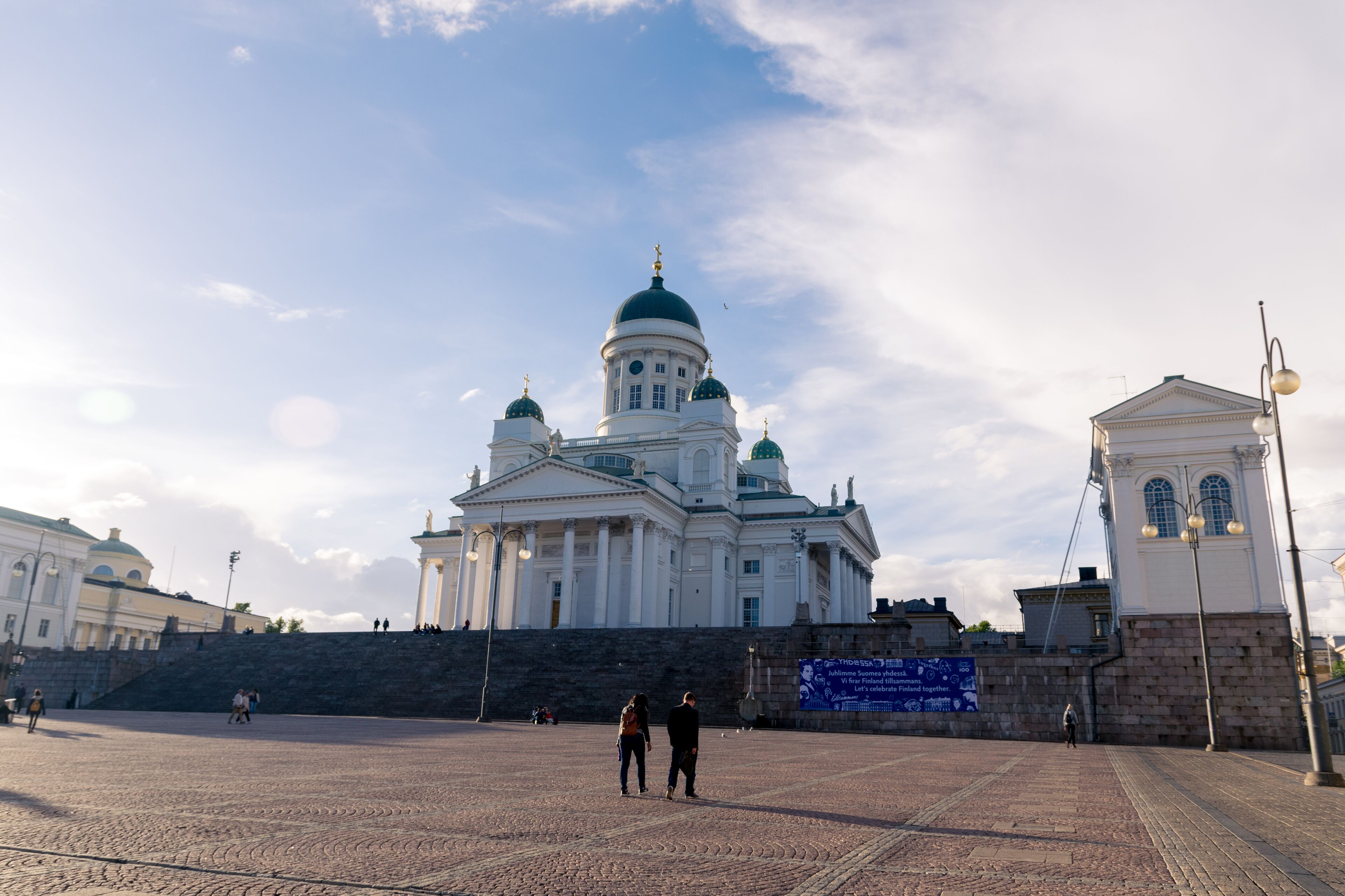A large open plaza with a historic building featuring domes and columns.